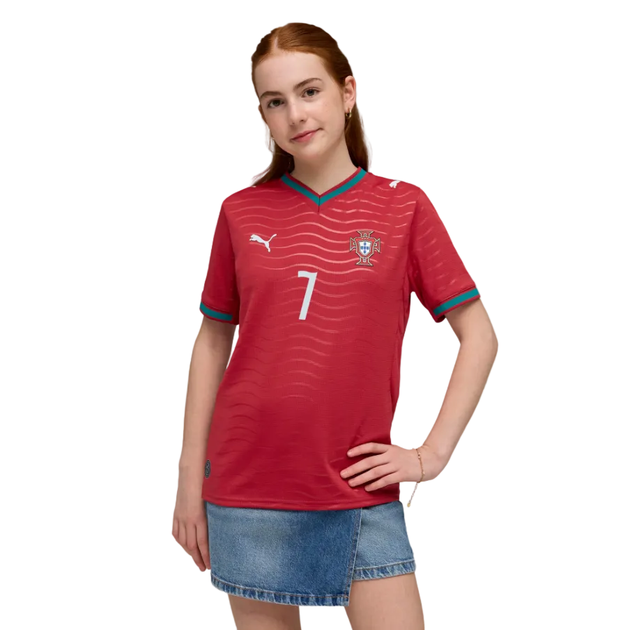 A young woman with red hair wears a red Portugal soccer jersey with number 7 and a denim skirt, posing against a black background.