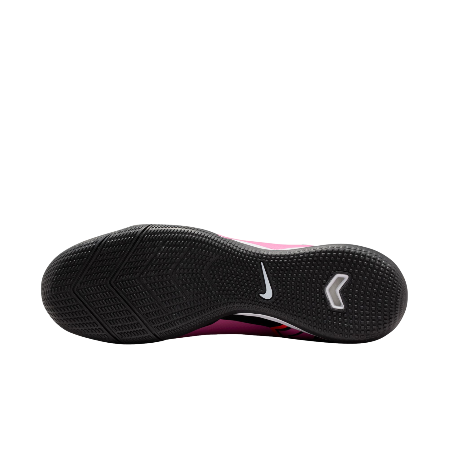 The textured black outsole of a pink Nike indoor soccer shoe, showing the tread pattern, a white Nike swoosh, and a white chevron-shaped logo.