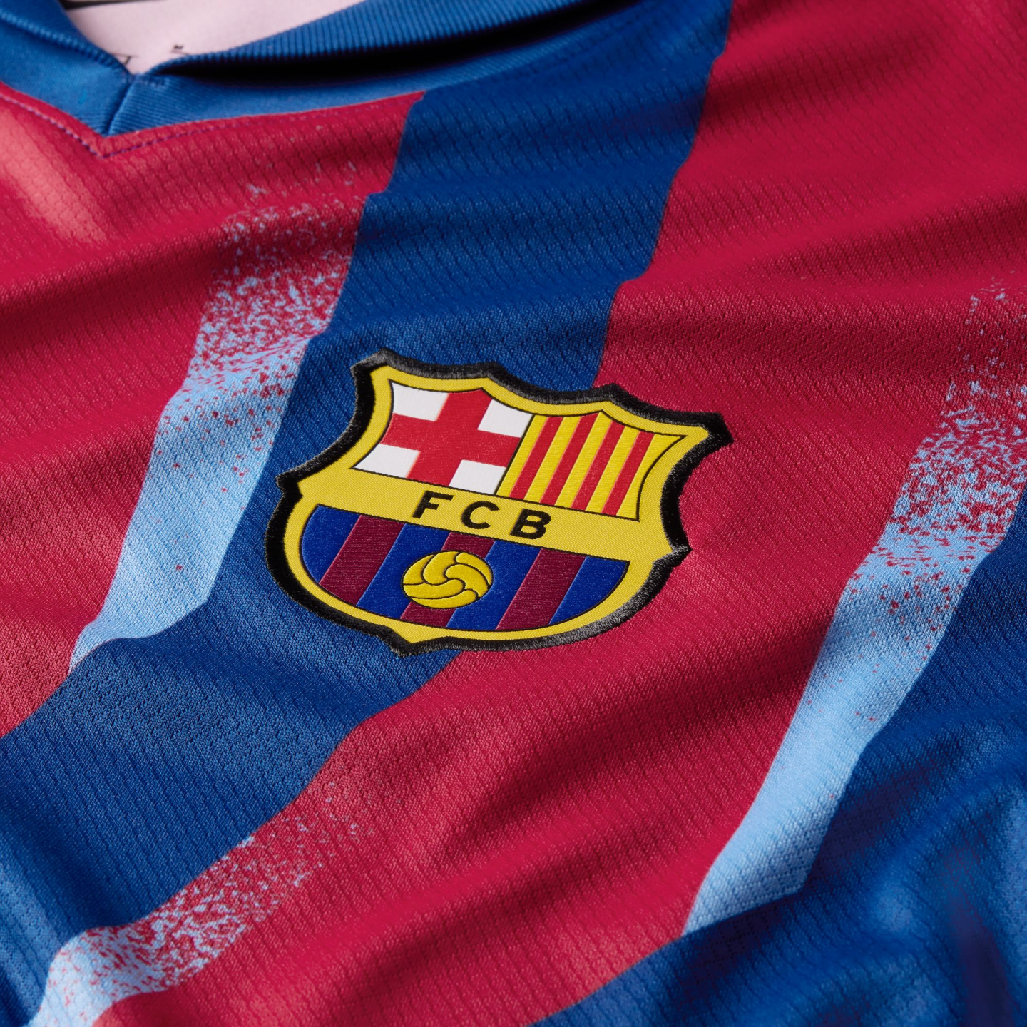Close-up of the FC Barcelona club crest on a blue and maroon striped jersey with a textured fabric.