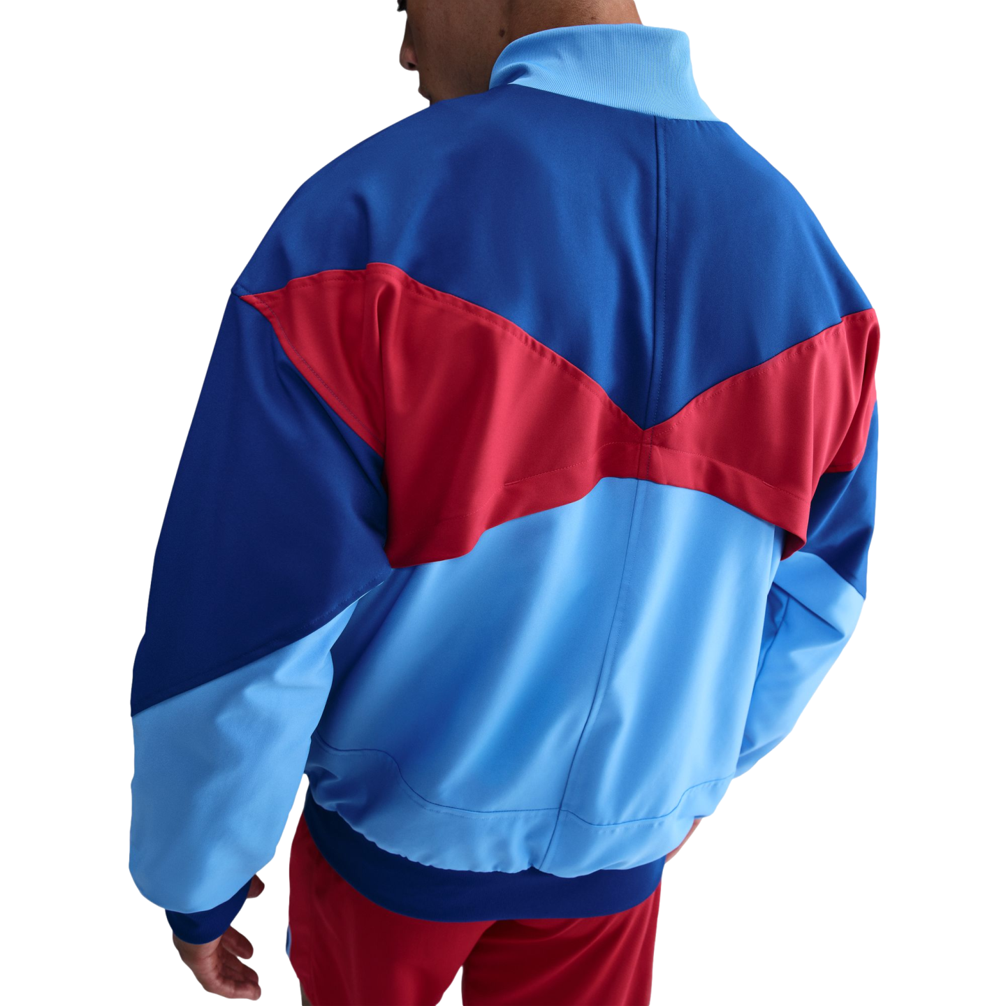 Rear view of a royal blue, light blue, and red color-blocked track jacket with geometric panels, worn with matching red shorts against a black background.