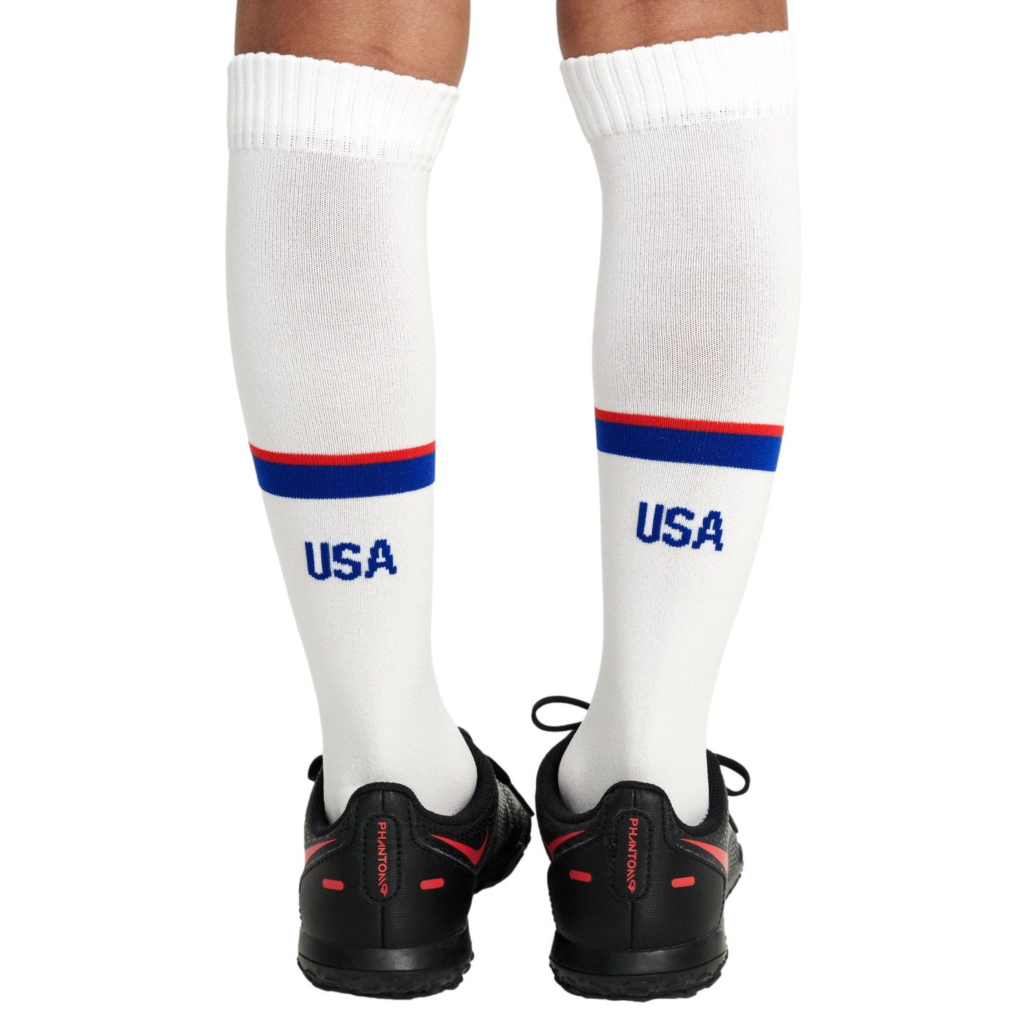 Rear view of a person's legs wearing white knee-high USA socks with red and blue stripes and black Nike Phantom soccer shoes.