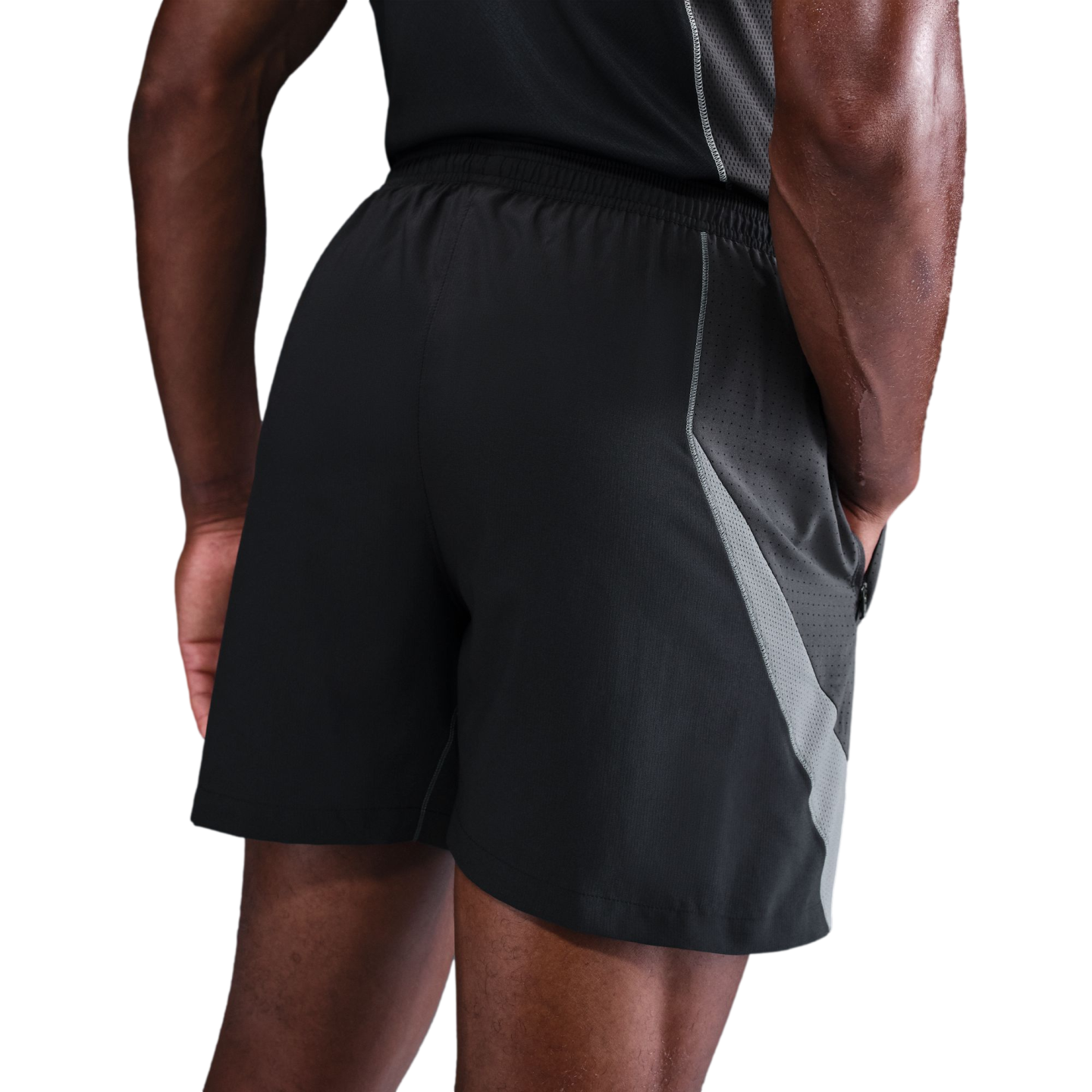 Rear view of a person wearing black athletic shorts with grey mesh side panels and a matching black tank top against a black background.