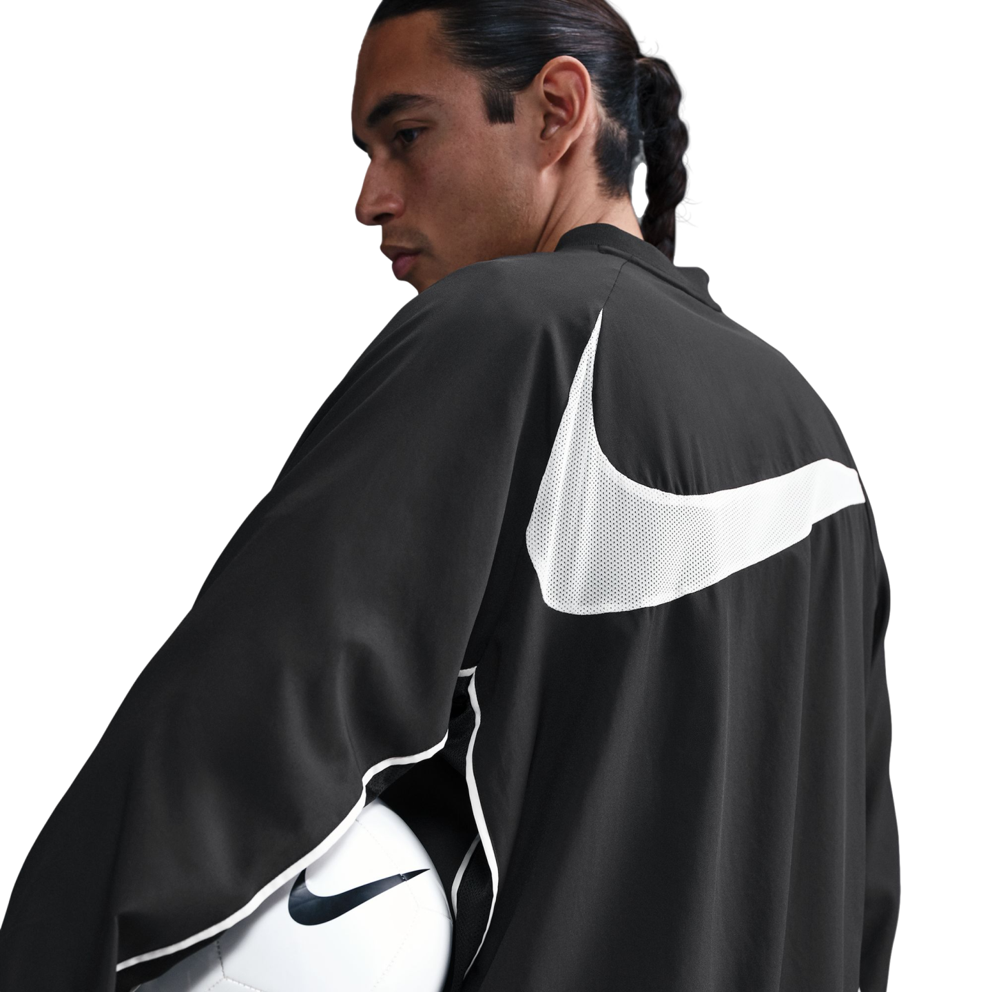Man with a braid in a black Nike jacket with a large white swoosh on the back, holding a soccer ball. White background.