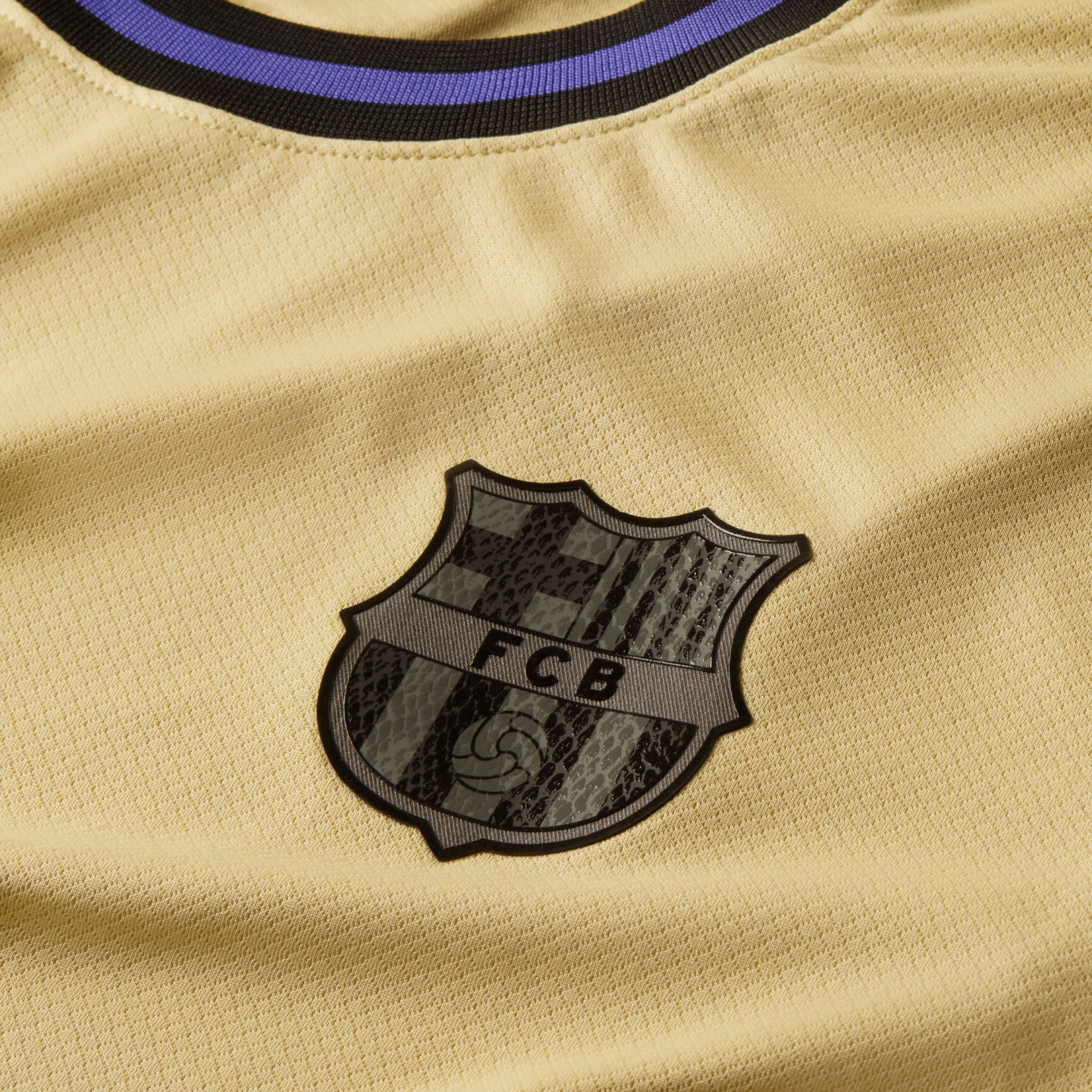 Close-up of a gold mesh soccer jersey featuring a black and gray FC Barcelona crest and a black and purple striped collar.