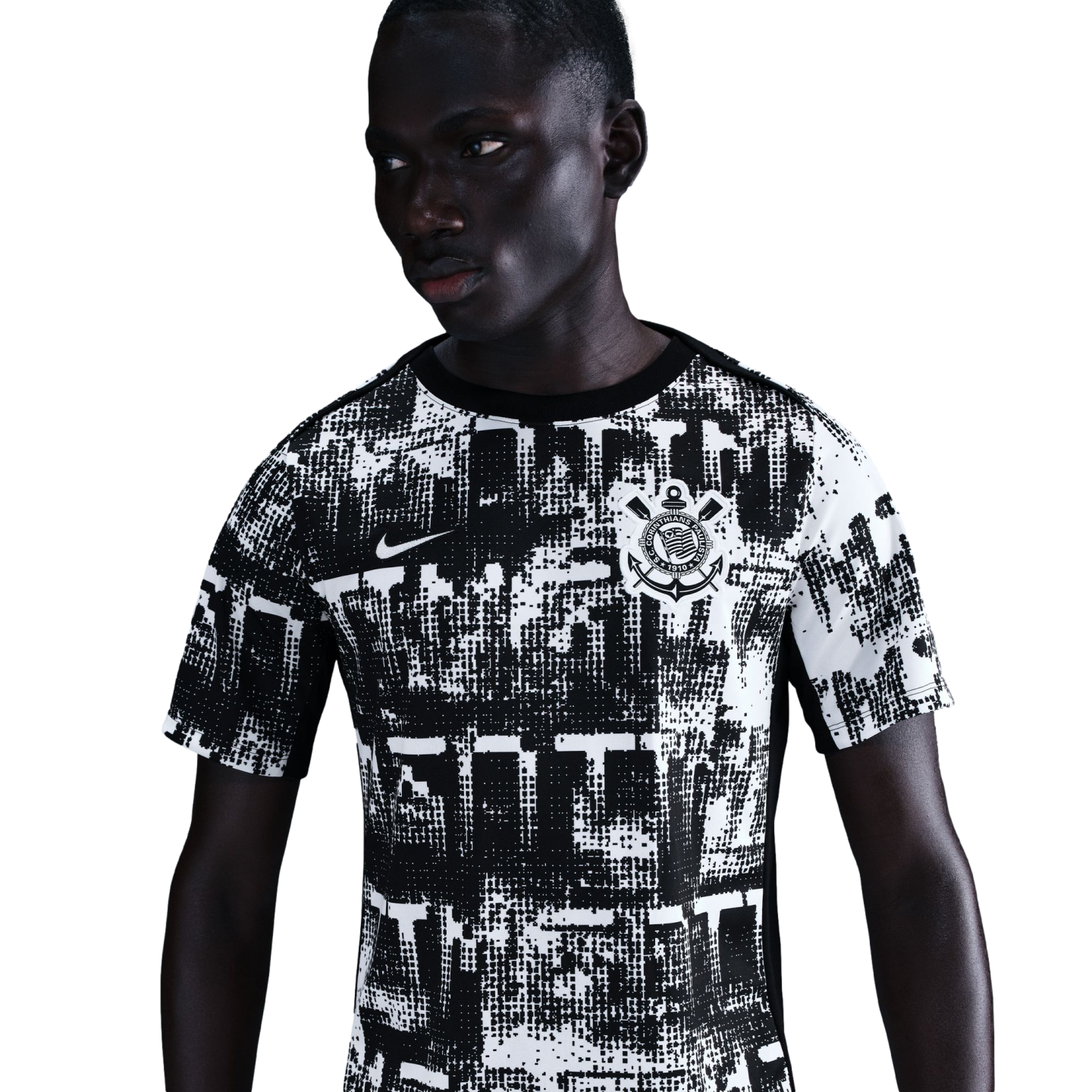 A dark-skinned man wearing a black and white abstract print Nike Corinthians soccer jersey against a solid black background.