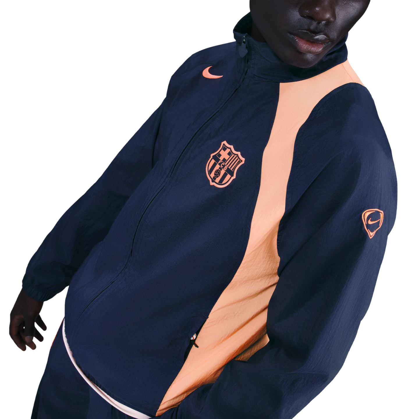 A person wearing a navy blue Nike FC Barcelona windbreaker with peach accents and the team's crest on the chest.
