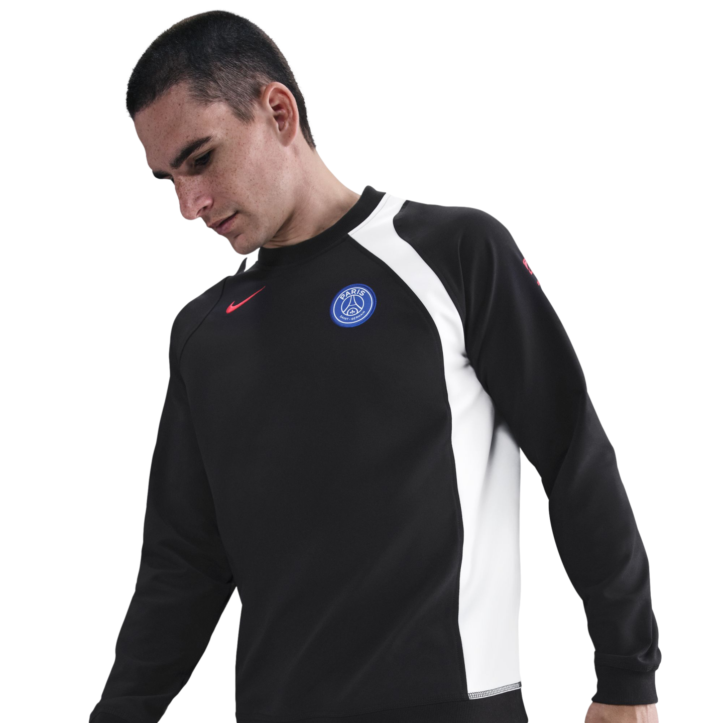 A man looking down while wearing a black and white Paris Saint-Germain long-sleeve sweatshirt with a red Nike logo against a black background.