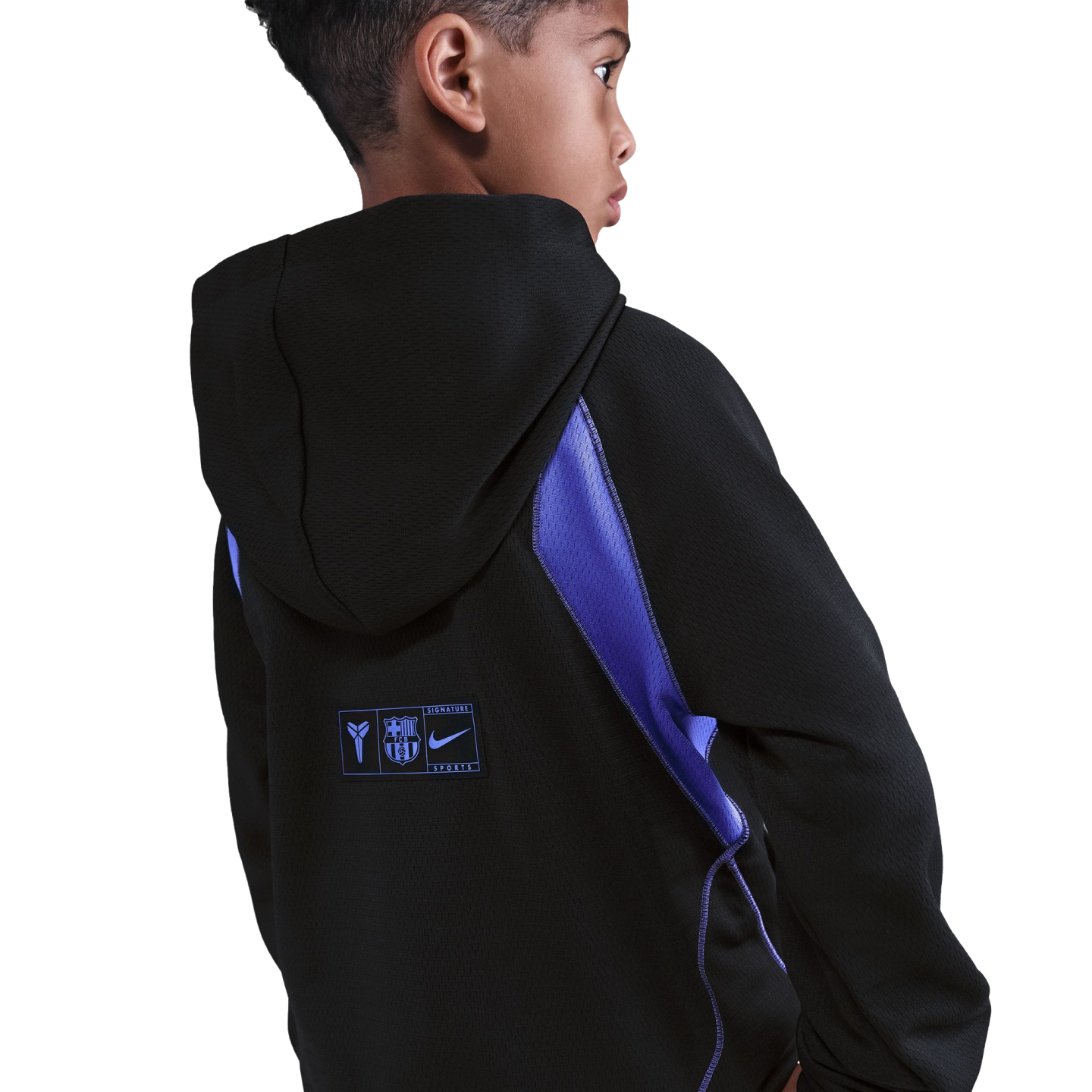 Back view of a boy in a black hoodie with blue mesh accents. A patch on the lower back features the Kobe Bryant, FC Barcelona, and Nike logos.