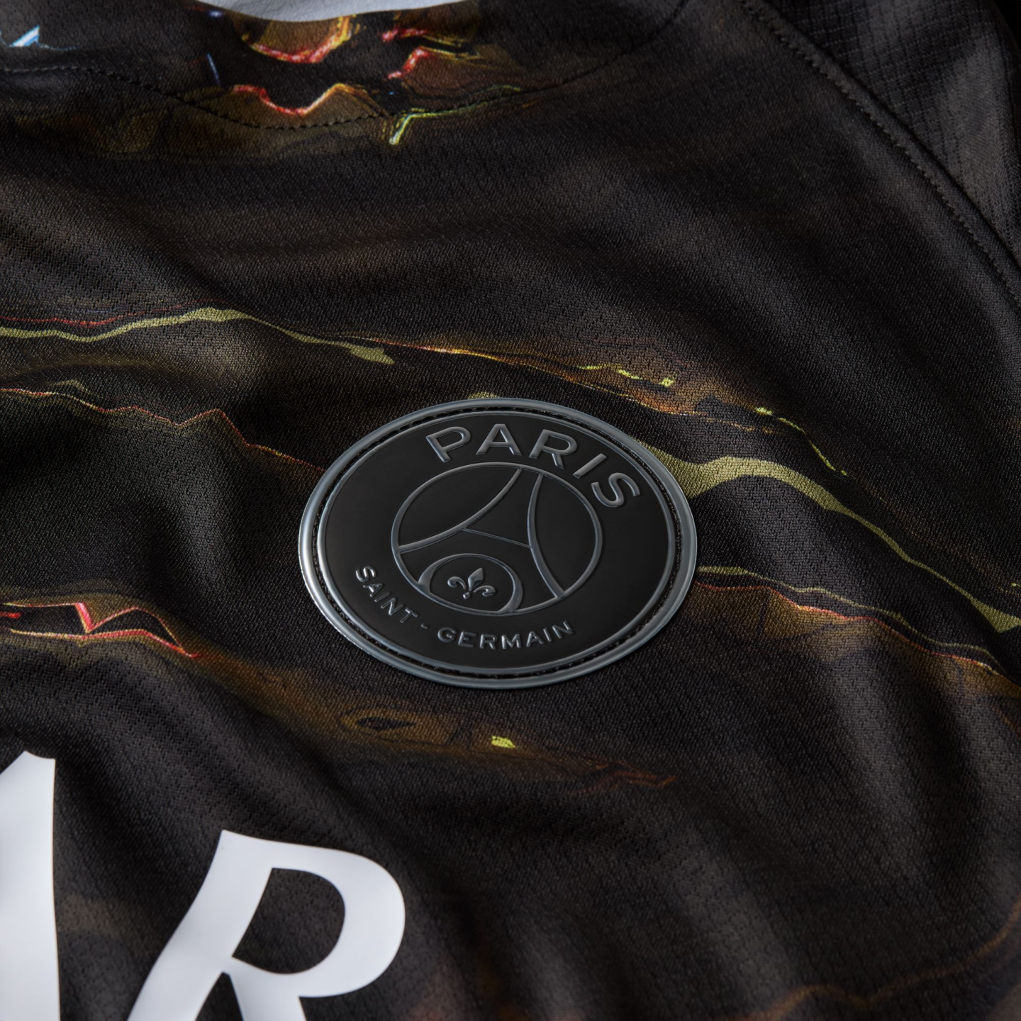 Close-up of a dark, marbled-pattern jersey featuring the Paris Saint-Germain club crest in a matte black and silver finish.