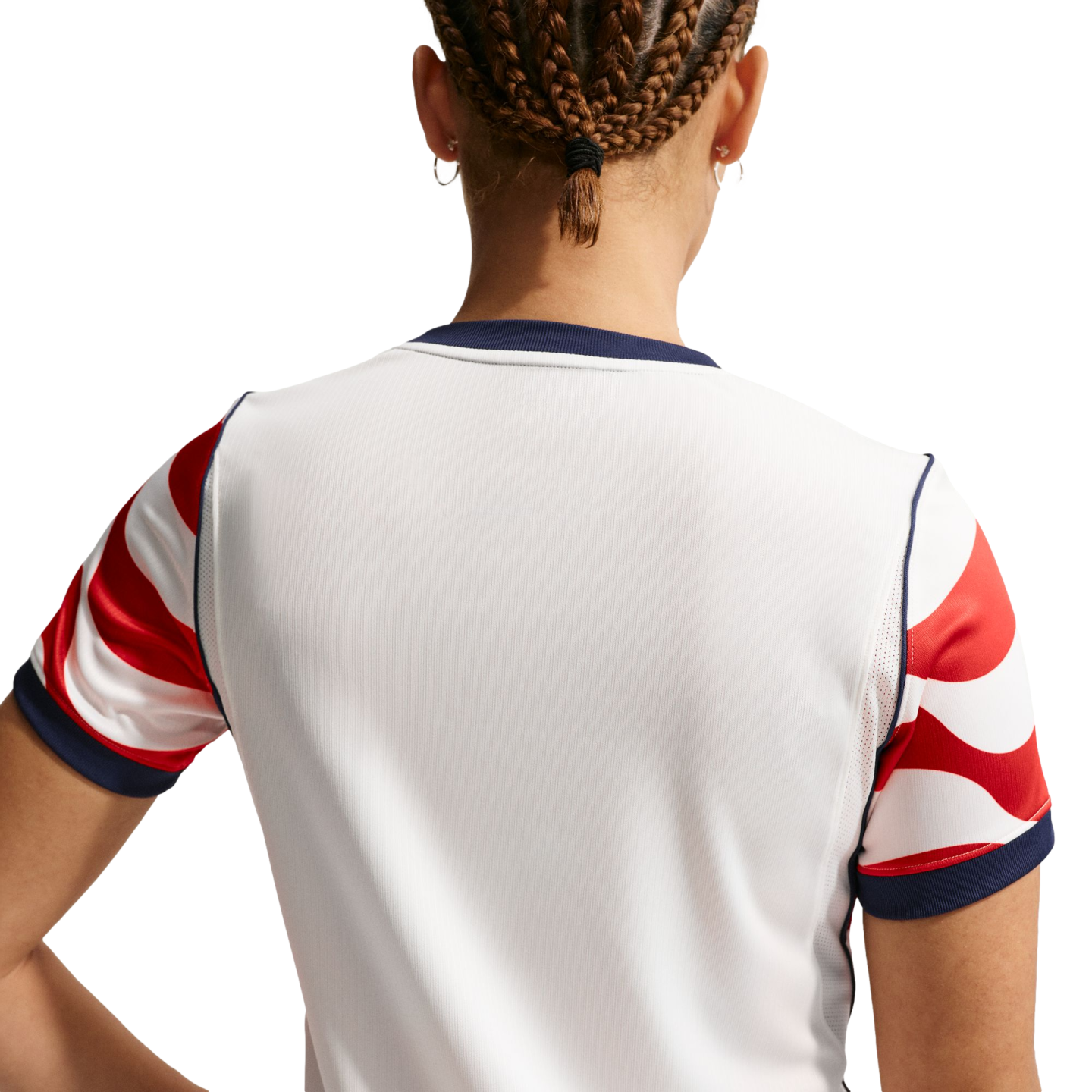Back view of a person with braided hair wearing a white sports jersey with red and white patterned sleeves and navy blue trim.