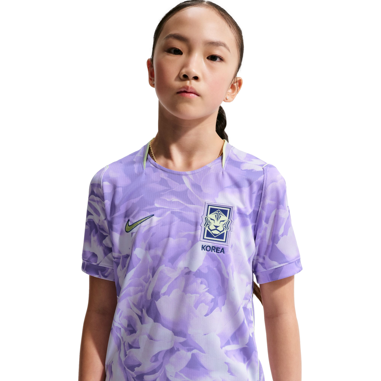 Portrait of a young girl wearing a light purple patterned Nike South Korea national team soccer jersey against a solid black background.