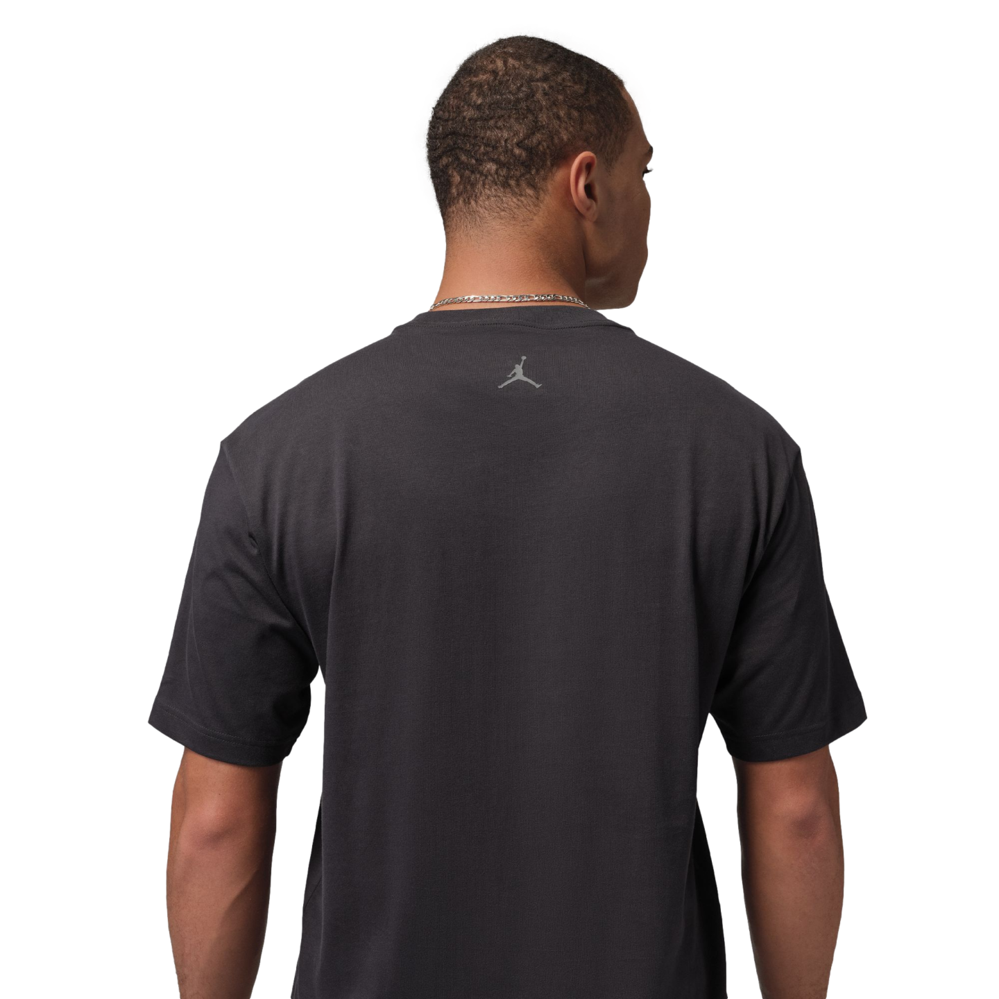 Rear view of a man wearing a charcoal gray Jordan t-shirt with a small silver Jumpman logo on the upper back. He is set against a solid black background.