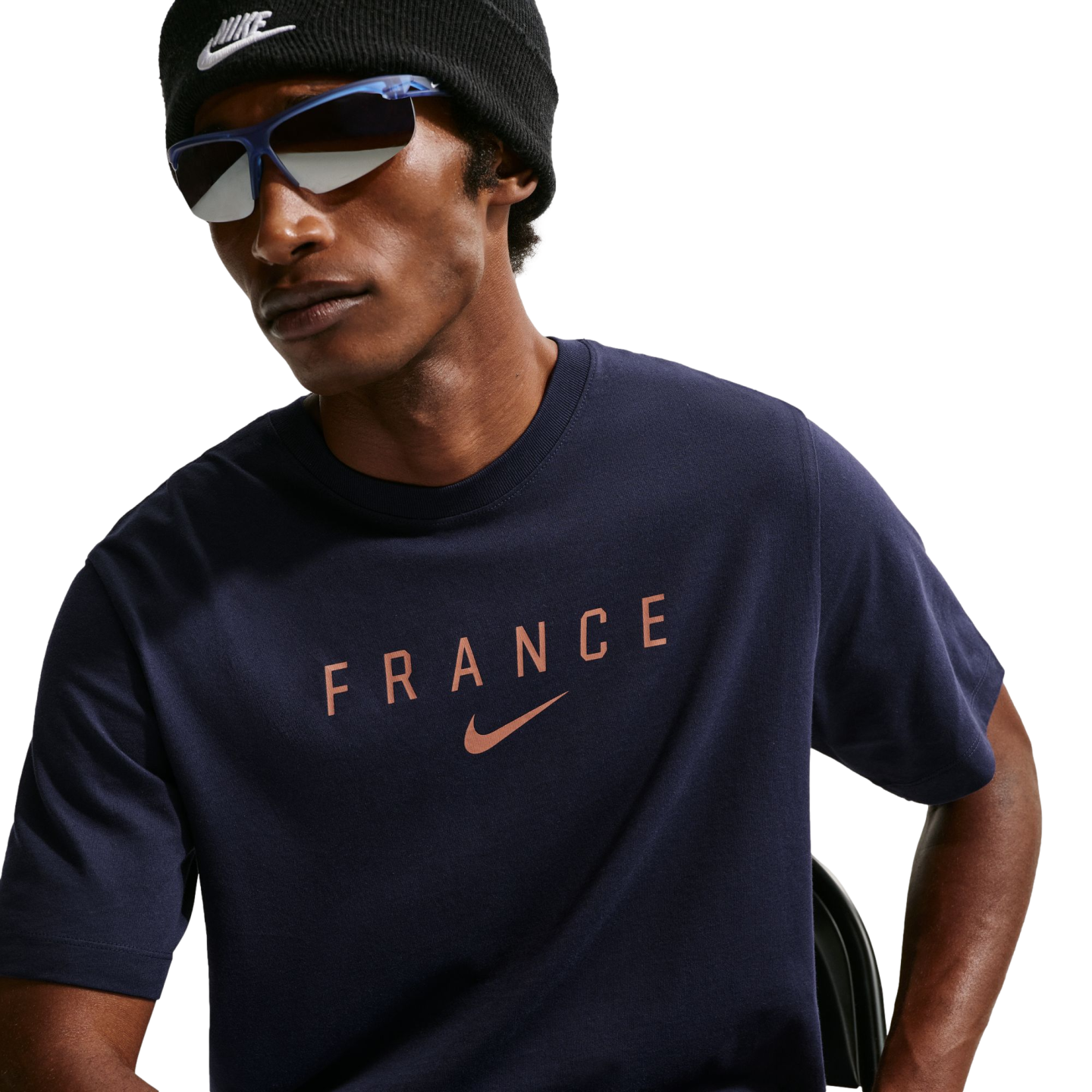 A person wearing a black Nike beanie and blue-framed sunglasses with a navy blue t-shirt featuring "FRANCE" and a rose-gold Nike logo.