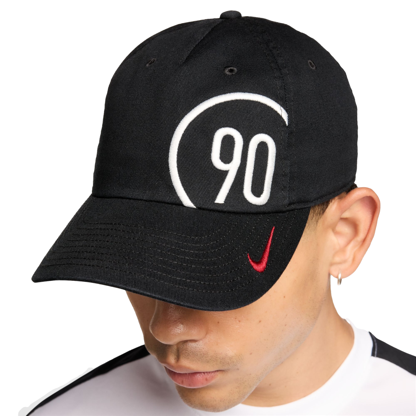 A person wears a black Nike cap with a large white '90' inside a circular border and a small red Nike swoosh on the brim.