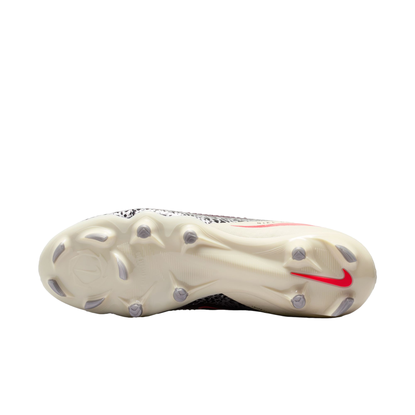 Underneath view of a Nike soccer cleat featuring a cream soleplate with grey studs, a red Nike swoosh, and a patterned upper against a black background.