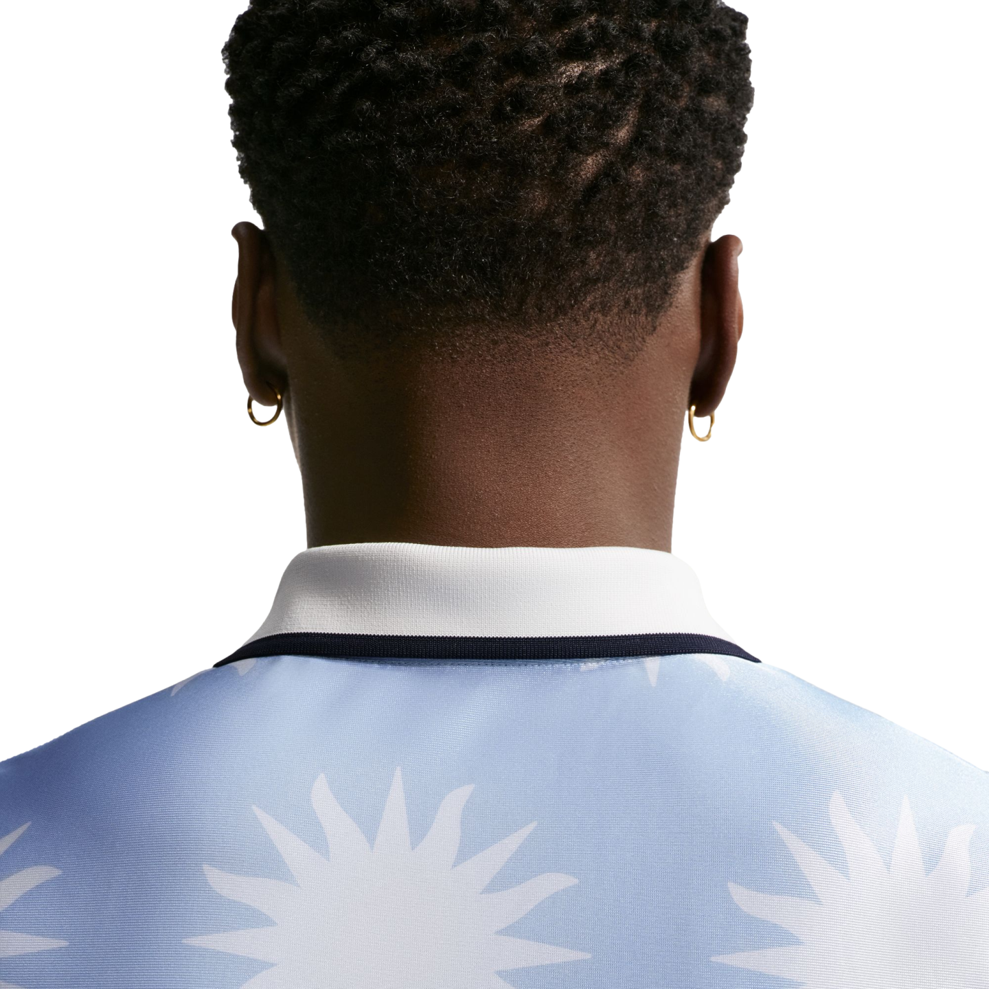 Back view of a person with short curly hair and gold hoop earrings, wearing a light blue polo shirt with a white sun pattern.