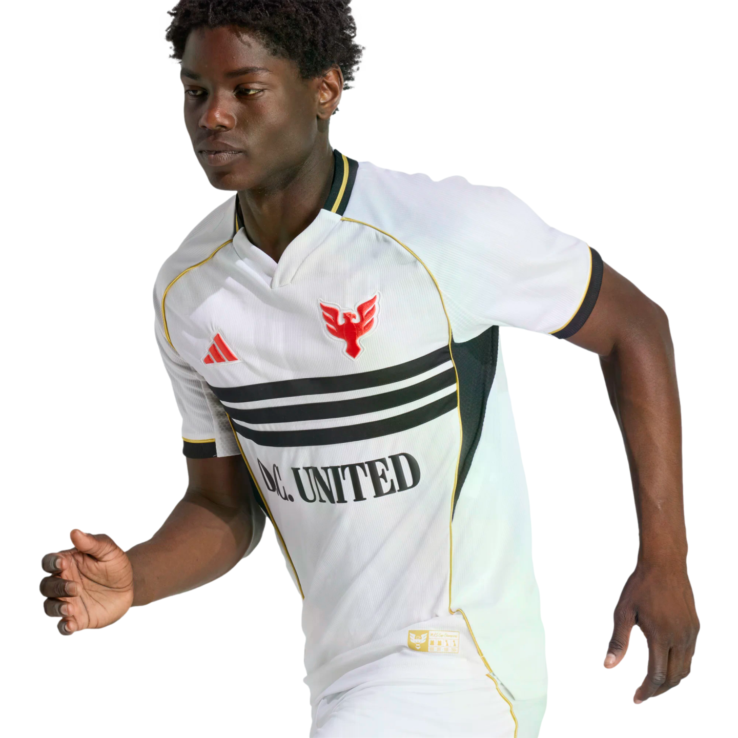 Young Black athlete in a white D.C. United soccer jersey with black stripes, gold trim, and a red eagle crest, captured mid-stride against a solid black backdrop.