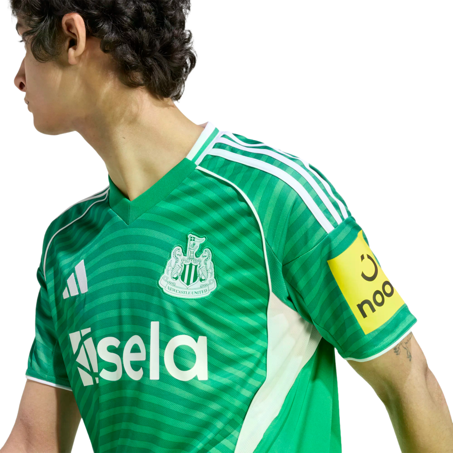 Person in a green Newcastle United football jersey with white Adidas stripes and Sela sponsor logo, shown in profile against a black background.