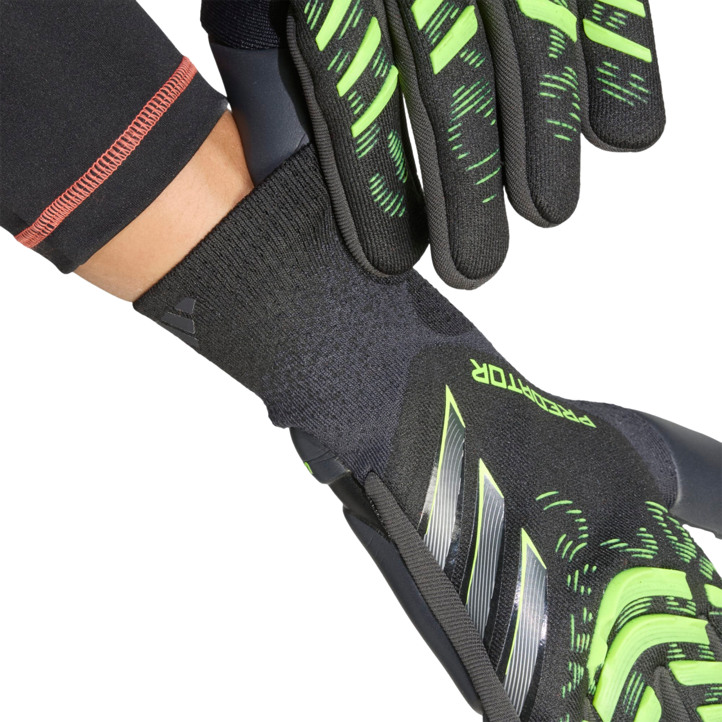 Close-up of black and neon green goalkeeper gloves being put on, highlighting the textured fingers and ribbed wrist cuff against a black background.