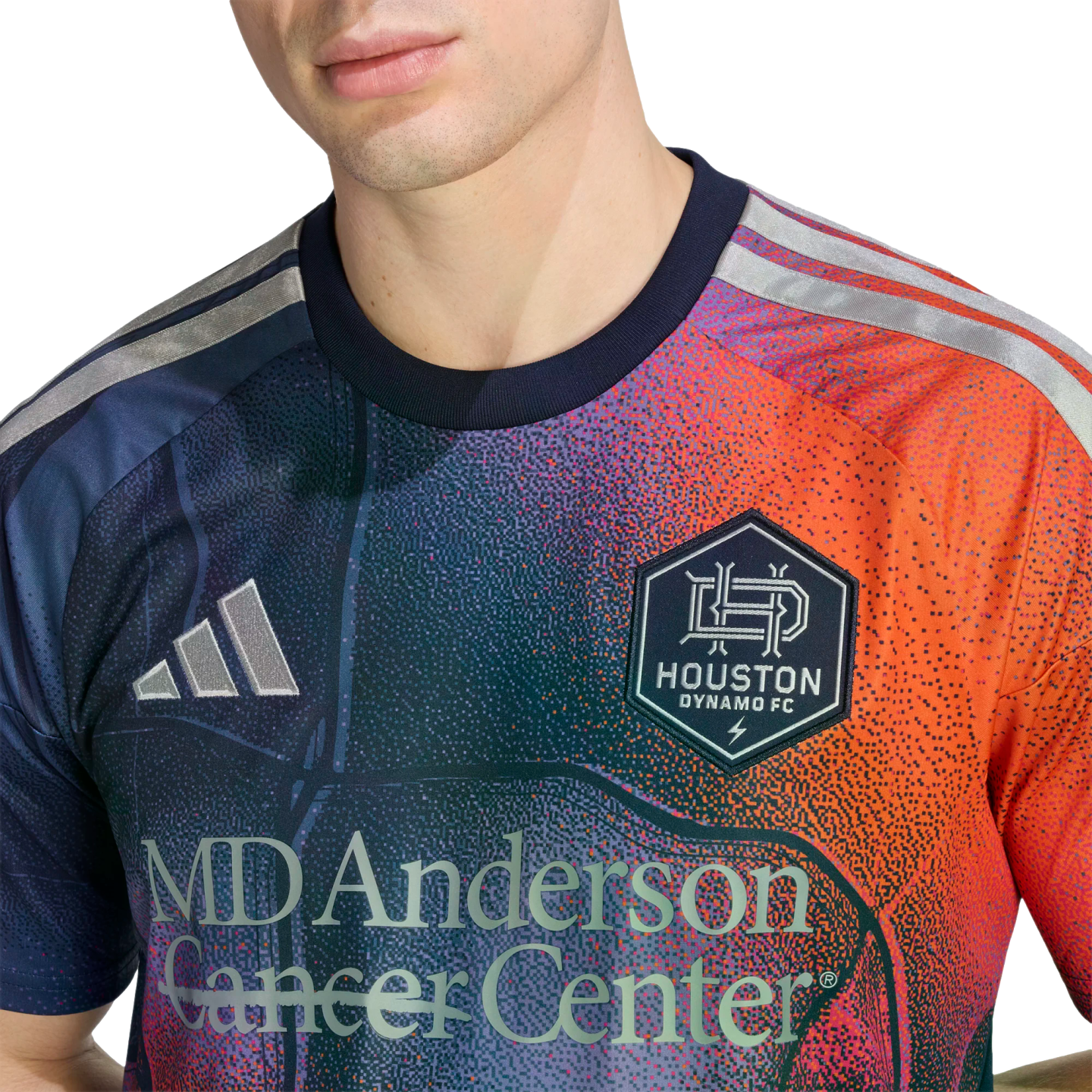 A person wears a Houston Dynamo FC soccer jersey with a pixelated blue-to-orange gradient, featuring the team crest, Adidas logo, and MD Anderson Cancer Center sponsorship.