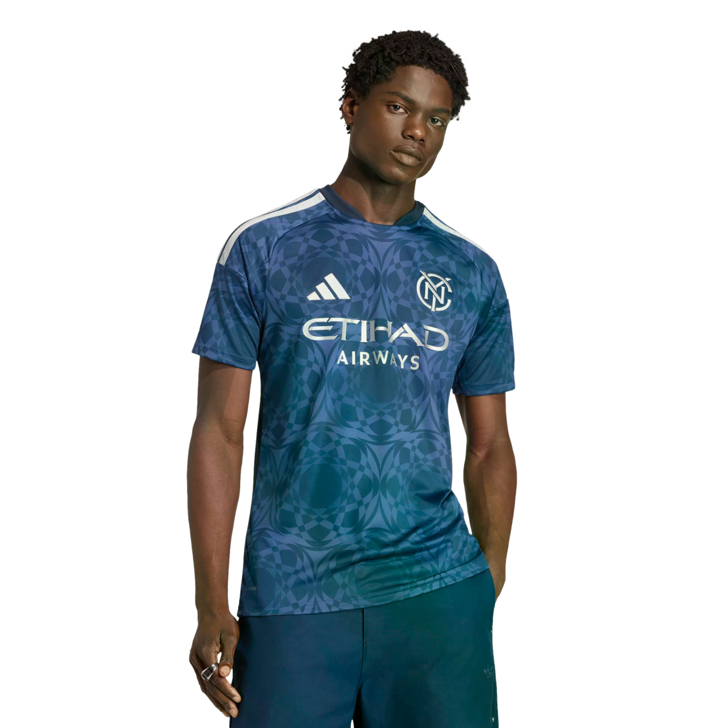 A man in a blue, geometric-patterned Adidas soccer jersey with "ETIHAD AIRWAYS" in white lettering on the front, and navy blue pants. He has dark hair and is looking directly at the camera.