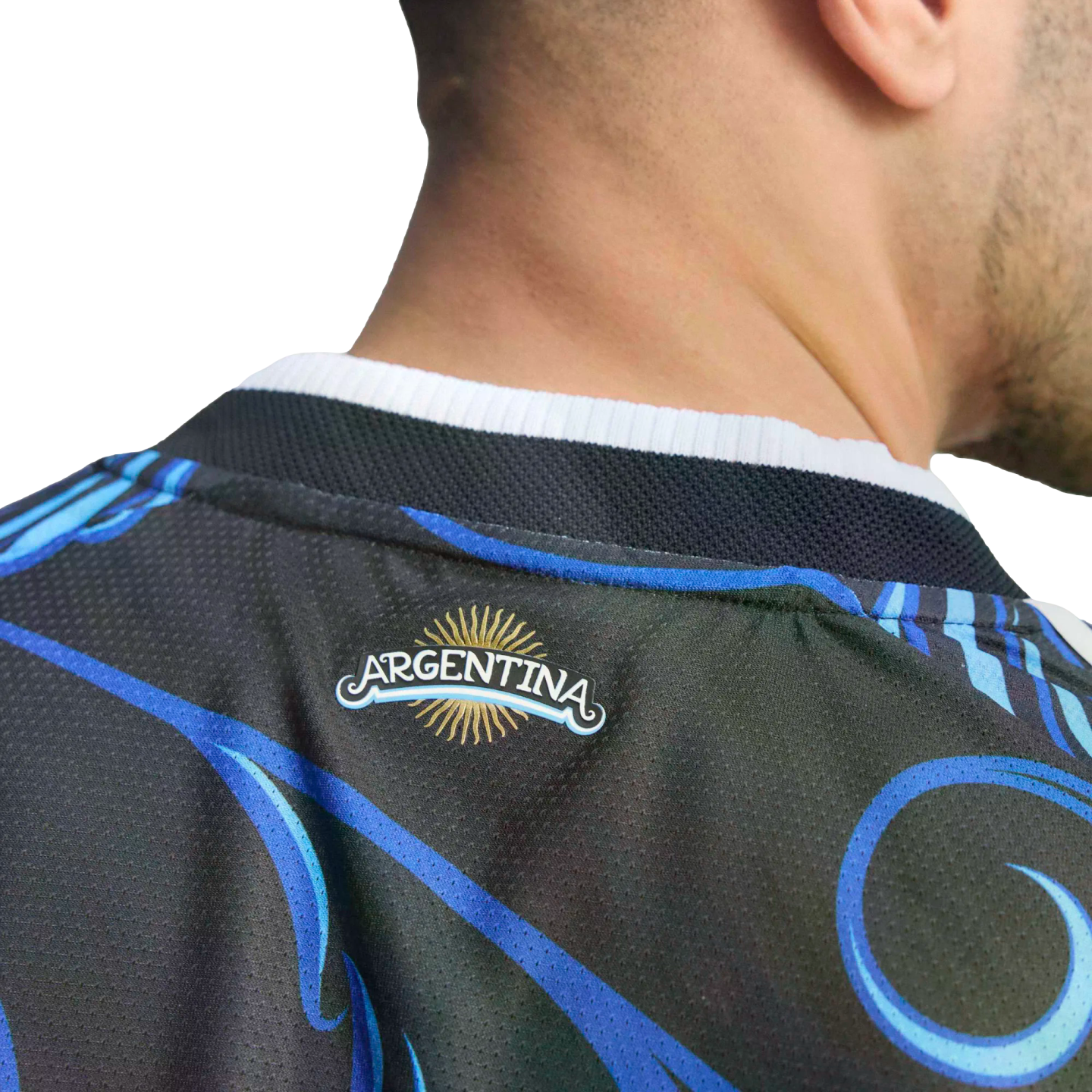Close-up of a person wearing a black jersey with blue swirls. A small logo on the back reads "ARGENTINA" beneath a golden sun. The background is solid black.