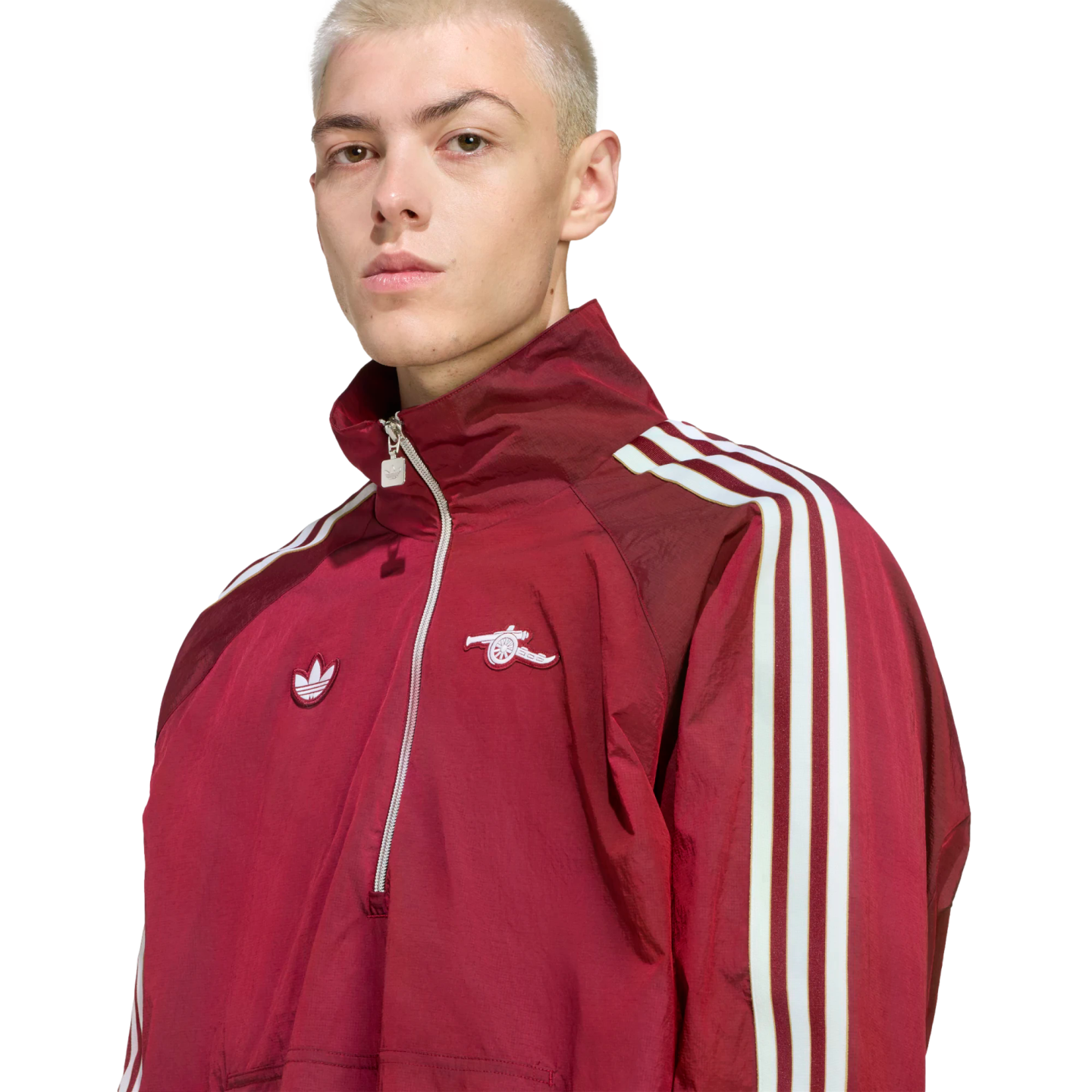 A blond man wears a maroon Adidas x Arsenal half-zip track jacket with white stripes on the sleeves, set against a black background.