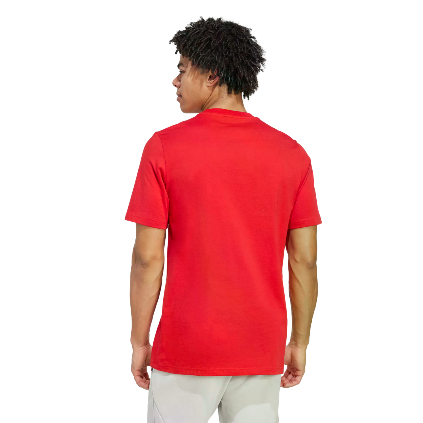 Rear view of a man with dark curly hair wearing a plain red T-shirt and light-colored pants, shown from the waist up against a black background.