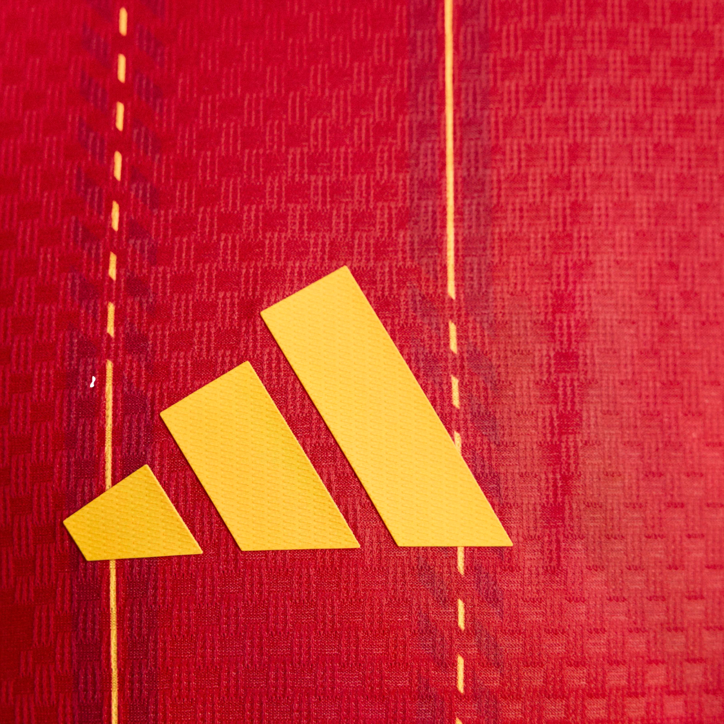 Yellow Adidas logo on a red textured fabric background with vertical yellow dashed lines.