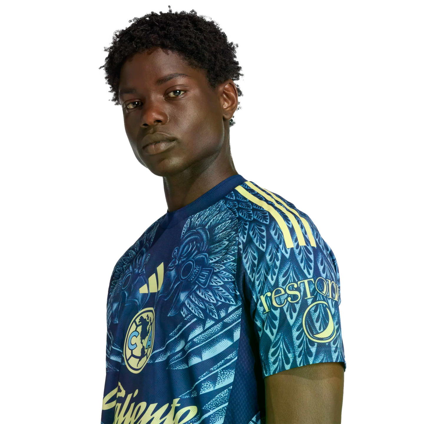 A Black man with short curly hair wears a patterned blue and yellow soccer jersey, looking at the camera against a black background.