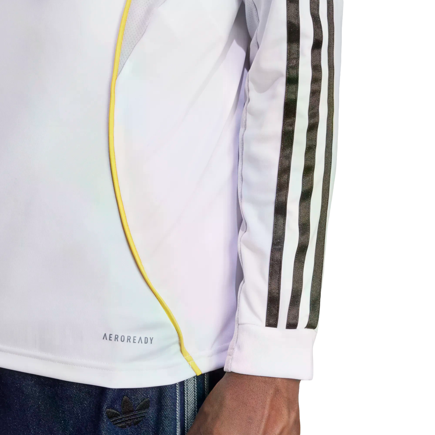 Side view of a white long-sleeve athletic shirt featuring black stripes on the sleeve, a yellow curved accent line, and "AEROREADY" text near the bottom hem.