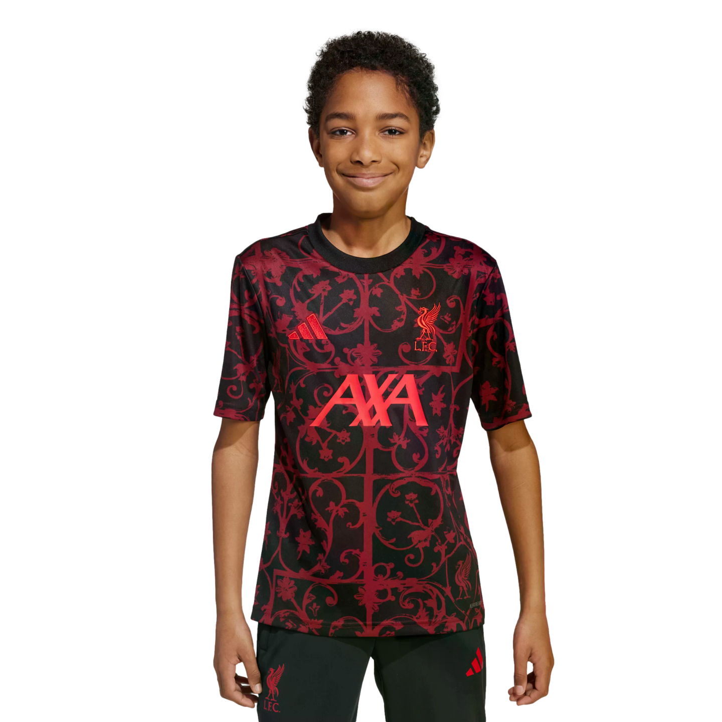 A young boy wearing a red and black patterned Liverpool FC training jersey, smiling against a solid black background.