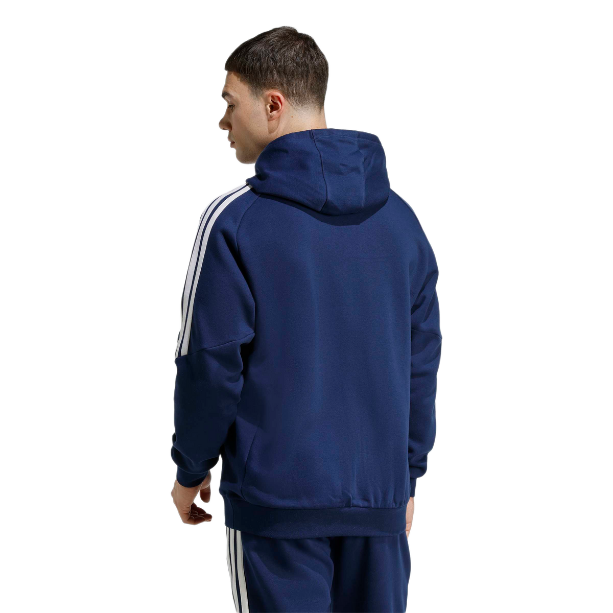 A man from the back wearing a navy blue Adidas zip-up hoodie and matching joggers, both featuring the iconic white three-stripes down the sides.