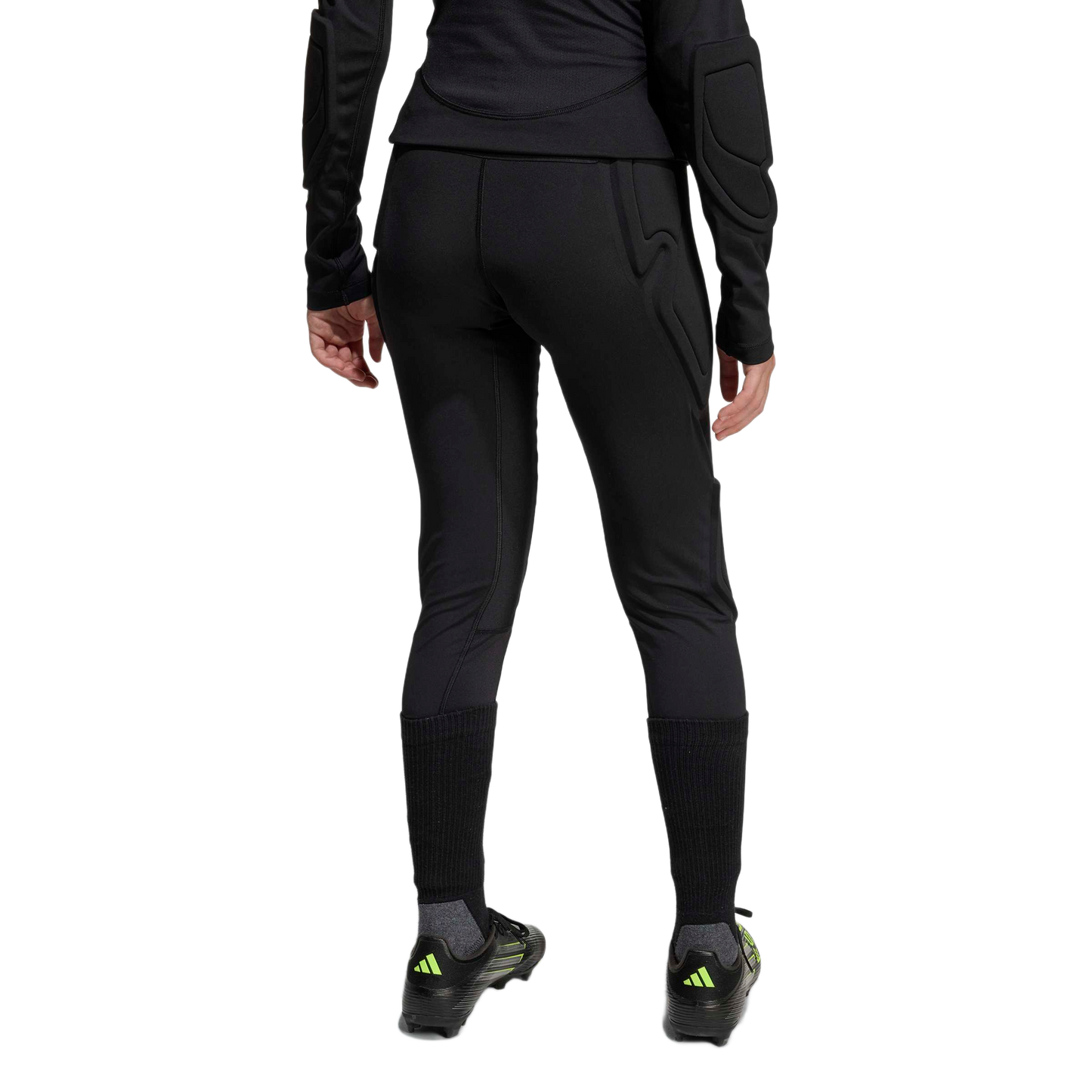 Rear view of a person wearing black padded athletic leggings, a long-sleeve padded top, tall black socks, and soccer cleats against a plain white background.