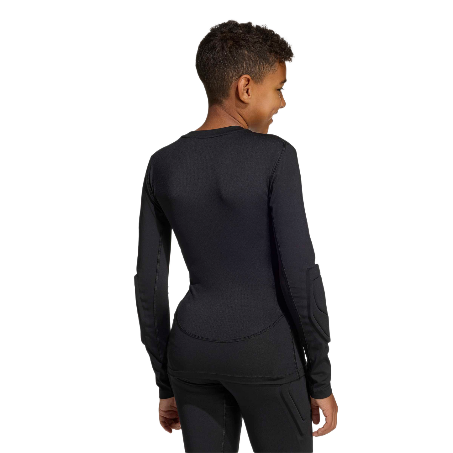 Back view of a youth in a black long-sleeved padded athletic shirt and matching pants, smiling over their shoulder against a plain background.