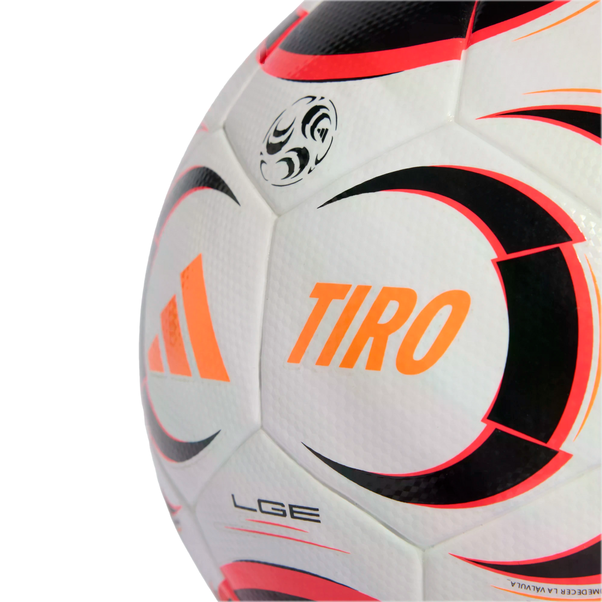 A close-up of a white Adidas Tiro soccer ball with orange, black, and red graphics on its textured surface against a black background.