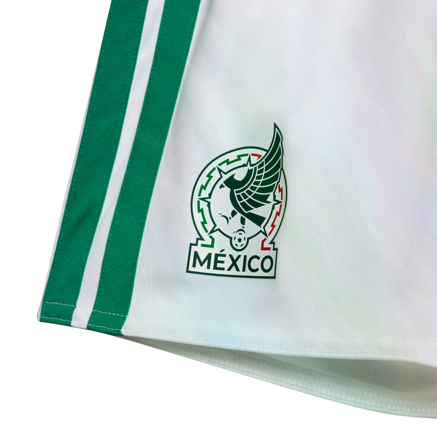 Close-up of white athletic shorts featuring two vertical green side stripes and the official Mexico national football team crest.