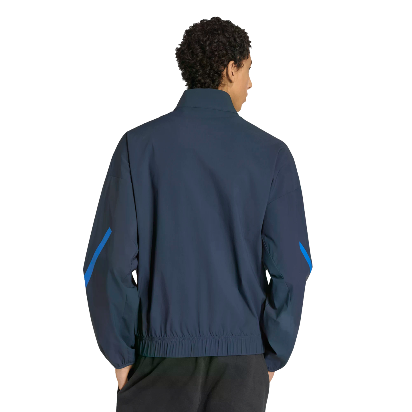 Back view of a person with dark curly hair wearing a navy blue track jacket with bright blue sleeve accents and black pants, set against a solid black background.
