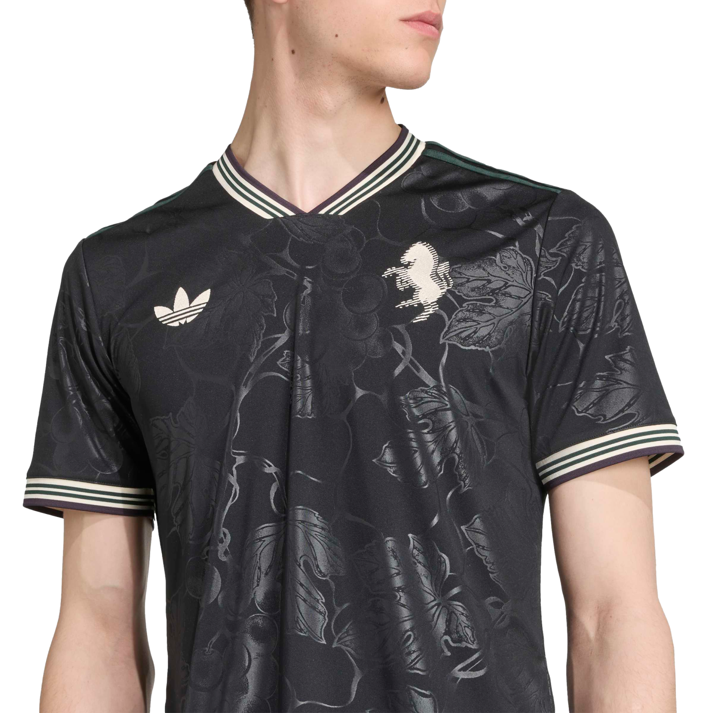 A man wearing a black Adidas jersey with a subtle floral tonal pattern, striped collar, Adidas Trefoil logo, and a lion crest on the chest.