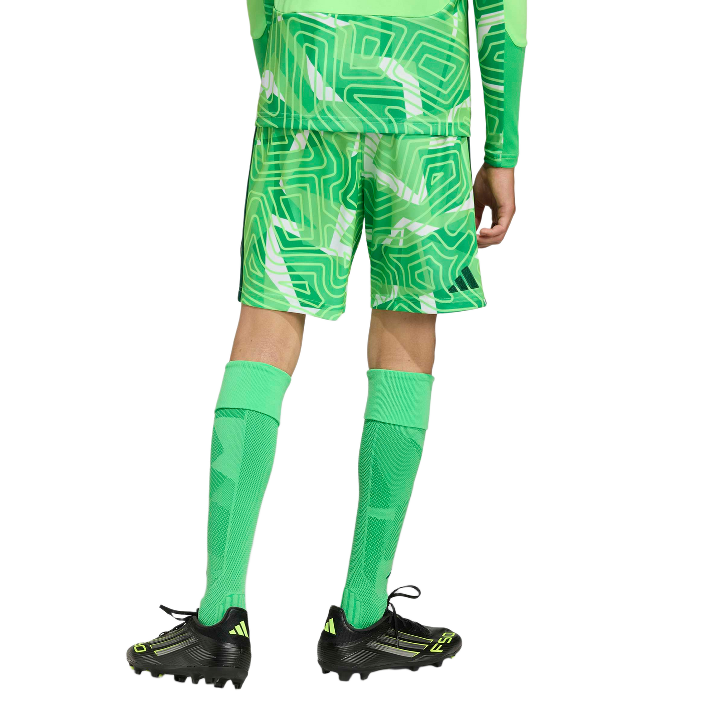 Rear view of a person wearing a green patterned soccer kit, tall green socks, and black and neon yellow soccer cleats against a light gray background.