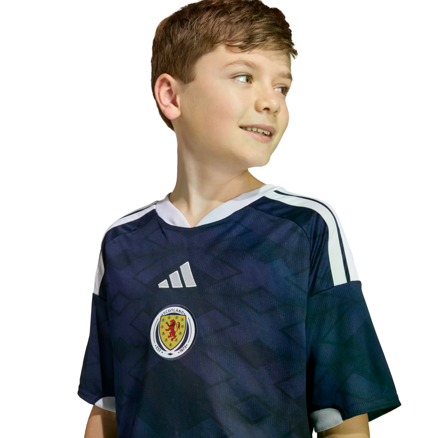 A smiling young boy wearing a navy blue Scotland soccer jersey with white stripes, looking to the side against a black background.