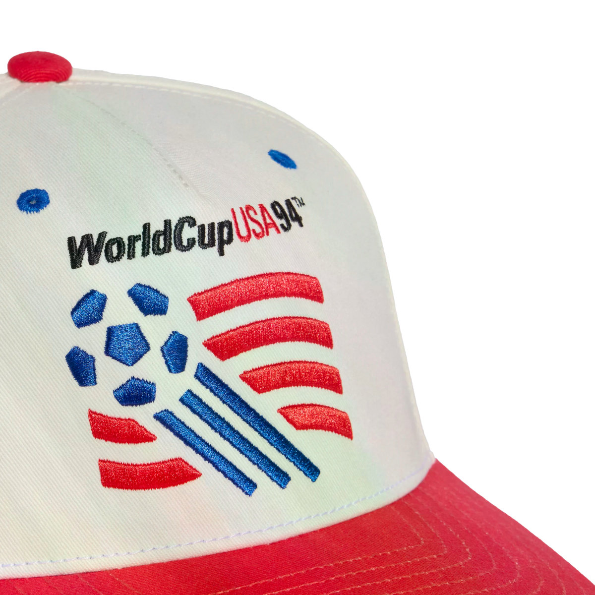 A close-up shot of a white baseball cap with a red brim featuring an embroidered logo for the 1994 FIFA World Cup. The logo includes the text "WorldCupUSA94™" above a graphic of a blue soccer ball with red stripes and blue motion lines.