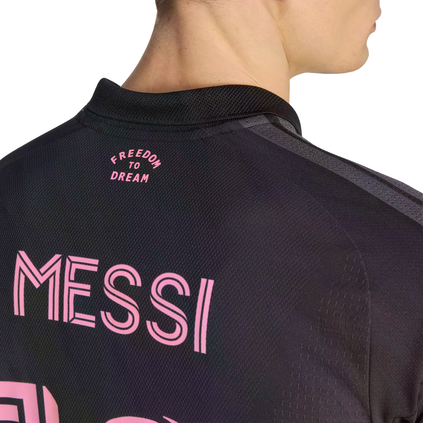 A close-up view from behind a person wearing a black jersey with pink lettering that reads "MESSI" across the back and "FREEDOM TO DREAM" near the collar.