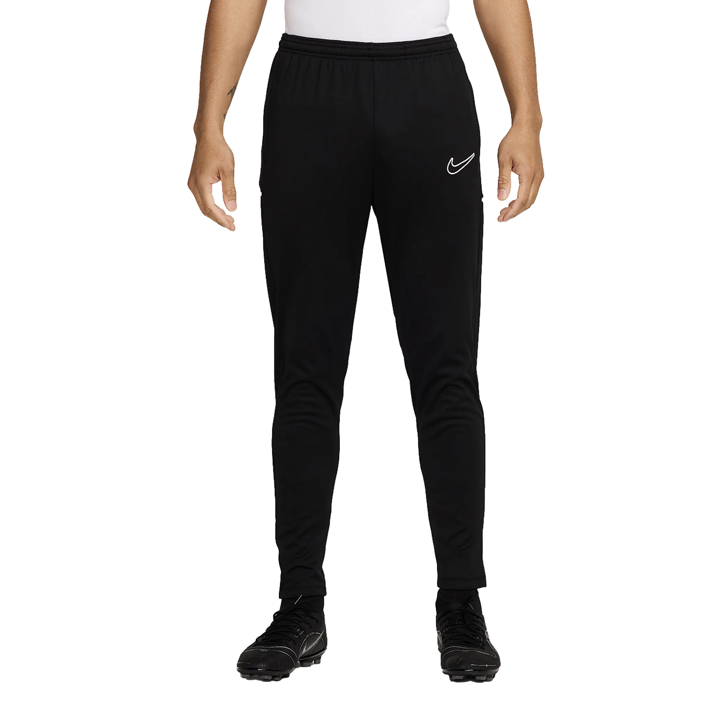 A person wears black Nike tapered training pants with a white logo and matching soccer cleats, standing against a plain white background.