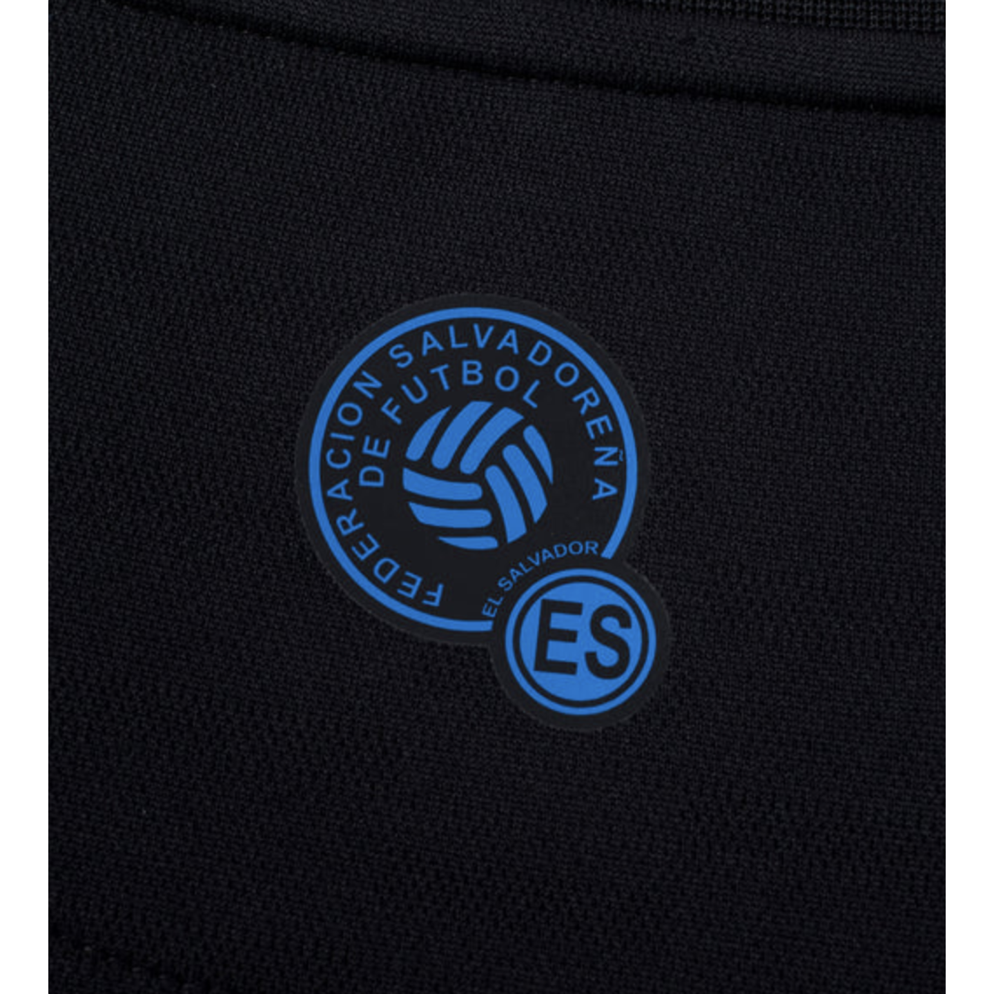 Blue and black El Salvador Football Federation crest featuring a stylized soccer ball and "ES" initials on dark textured fabric.