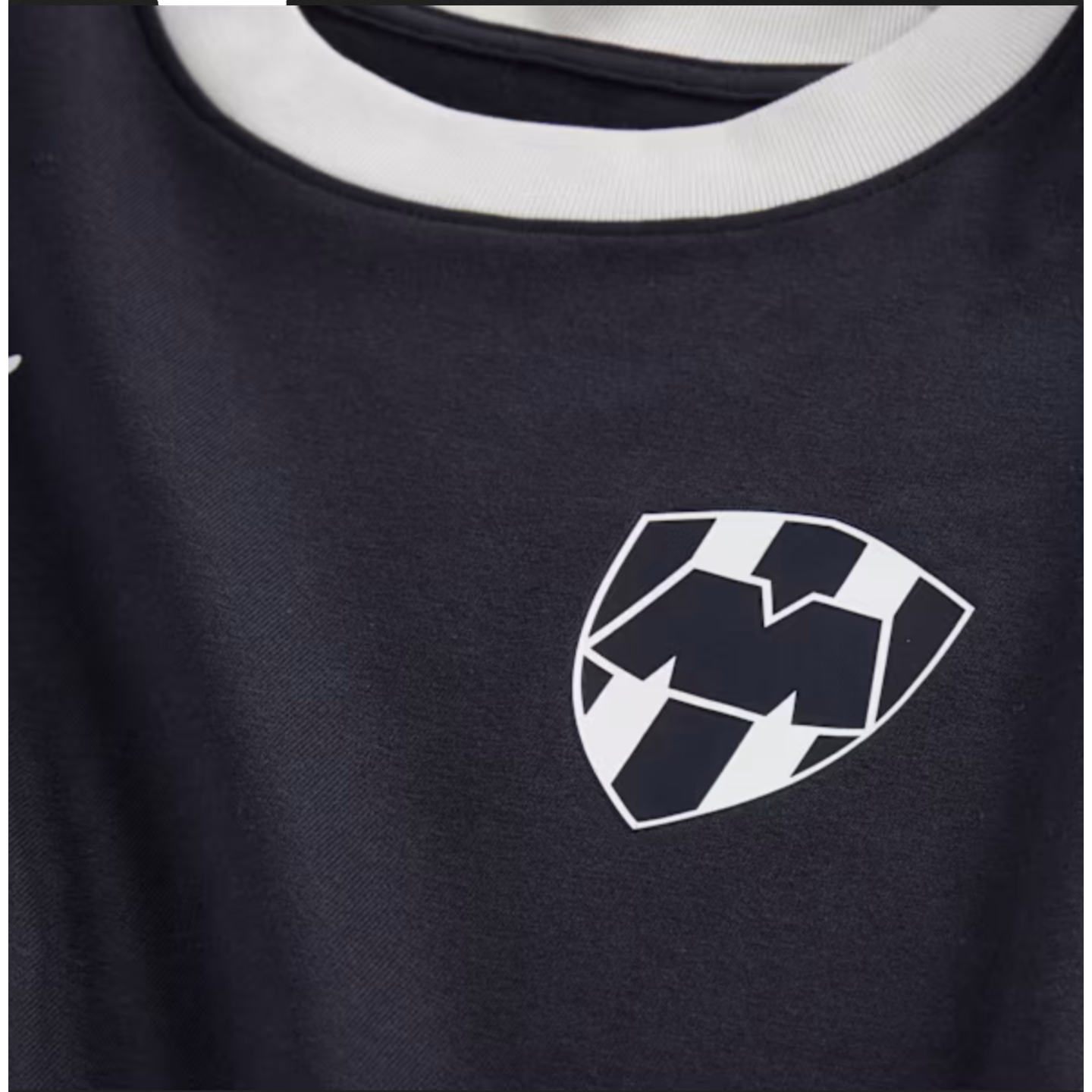 Close-up of a navy blue jersey with a white collar. On the chest is the C.F. Monterrey shield crest, featuring a stylized 'M' over vertical black and white stripes.