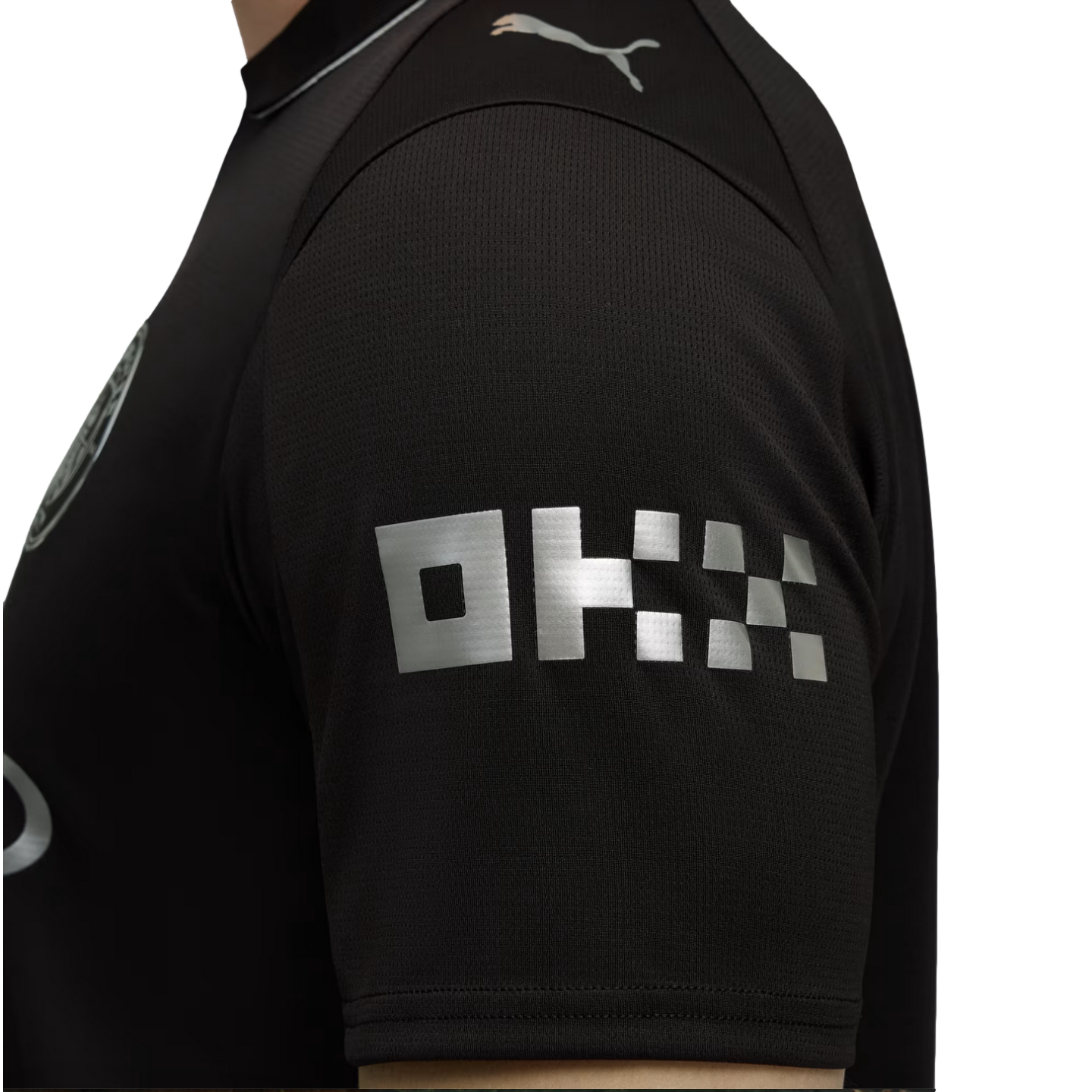 Close-up of a black jersey sleeve with a silver blocky "OKX" logo and a silver Puma logo on the shoulder.