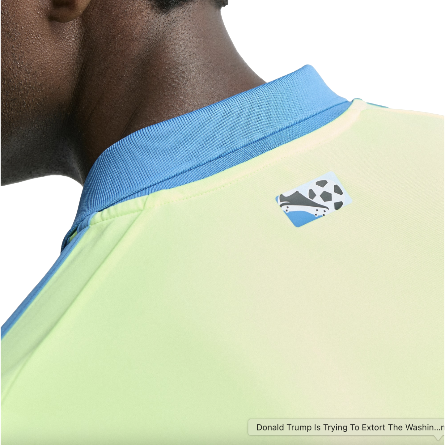 Close-up of a person's neck and shoulder wearing a lime green and blue athletic jersey with a small soccer cleat and ball logo on the back.