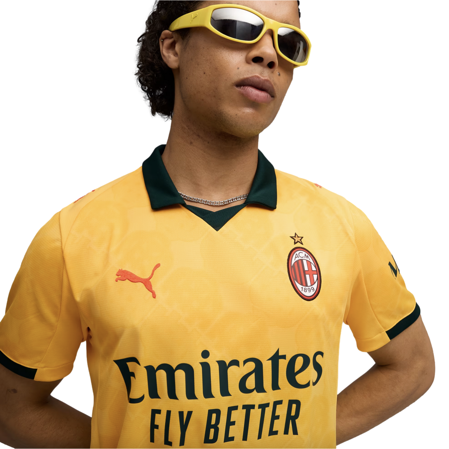 A man wearing a yellow AC Milan soccer jersey with a dark green collar and yellow-framed sunglasses against a solid black background.