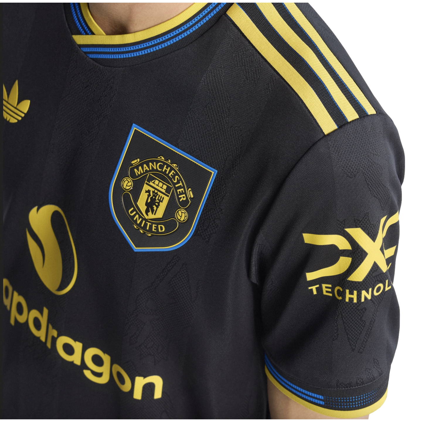 Close-up of a black and yellow Manchester United soccer jersey with the club crest, Snapdragon sponsor logo, and Adidas Trefoil logo.